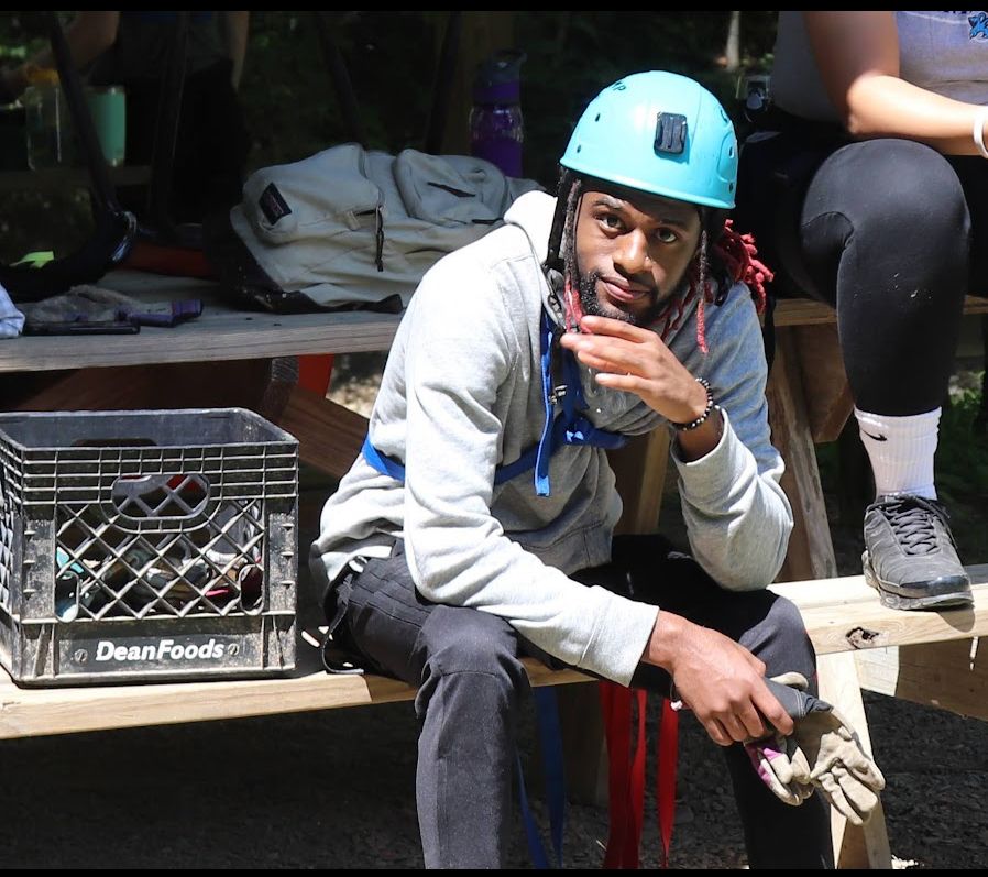 Taj Gregory with helmet sitting on a bench at Camp Akulana.